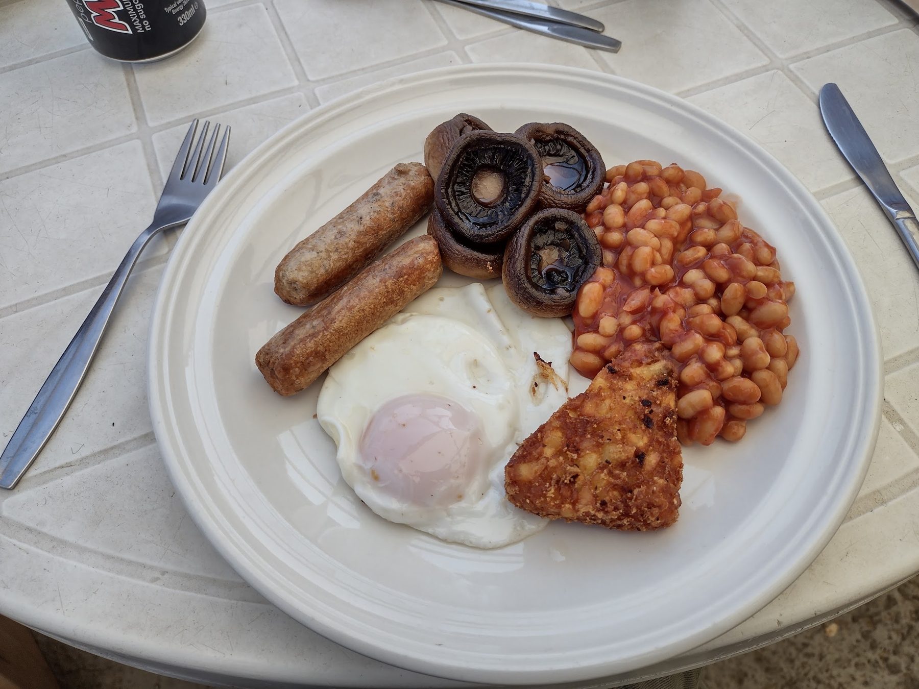 A cooked breakfast with sausages, egg, mushrooms, beans and fried bread
